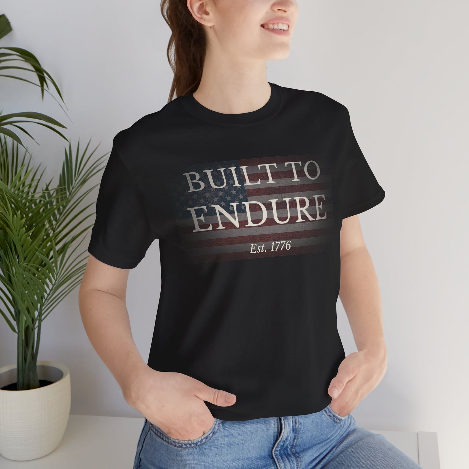 Built to Endure T-Shirt - Patriotic Est. 1776 Tee worn by a smiling model, featuring a minimal American flag design.