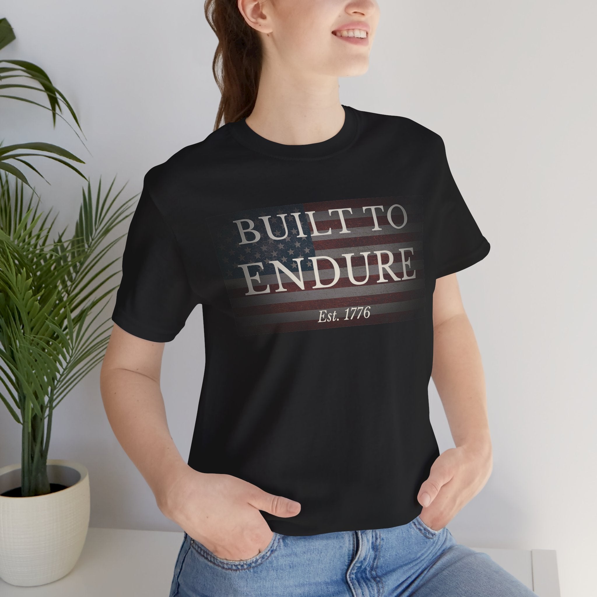 Built to Endure T-Shirt - Patriotic Est. 1776 Tee worn by a smiling model, featuring a minimal American flag design.